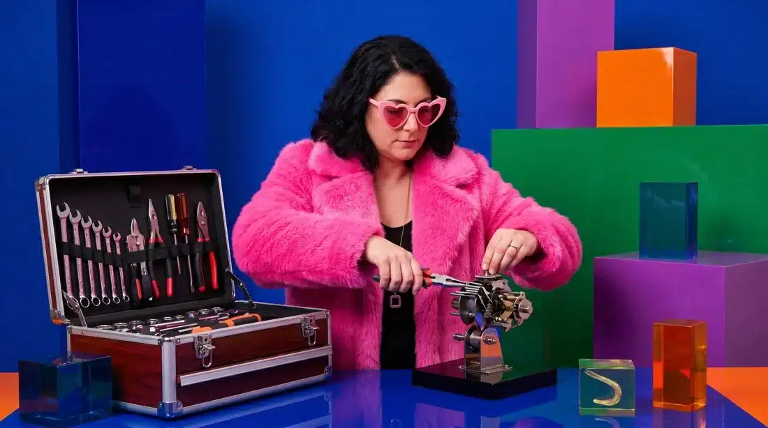 Yaelle David démonte un mécanisme avec sa caisse à outils, dans un décor coloré